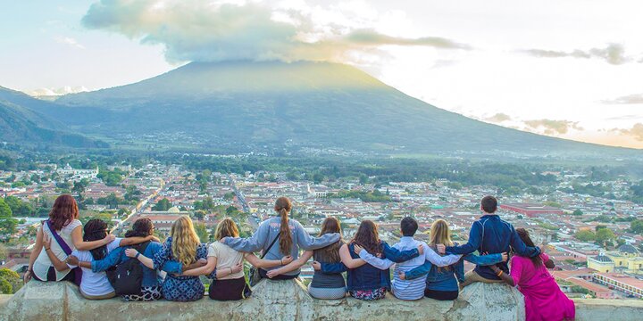 Study abroad students with their backs to the camera looking onto a town and volcano